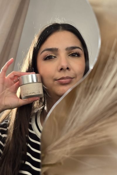 Valeria sosteniendo crema facial frente a un espejo, mostrando su rostro cuidado