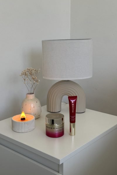 Varios productos de maquillaje (base, labiales, sombras) dispuestos sobre una mesa blanca minimalista.