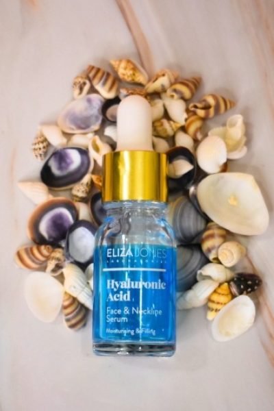 Serum de ácido hialurónico Eliza Jones con envase azul y dorado, rodeado de conchas marinas.