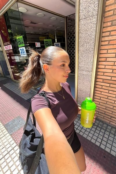 Marina Martínez con coleta haciendo selfie con botella de proteína BiotechUSA, mostrando su estilo de vida activo y saludable.