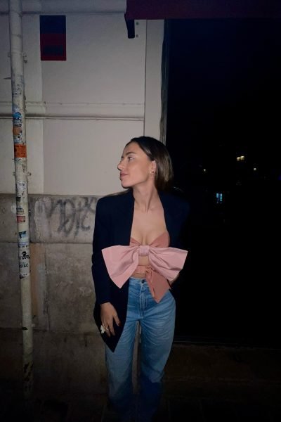 Noemí Prado con blazer negro, top rosa con lazo y jeans, posando de noche en una calle urbana.