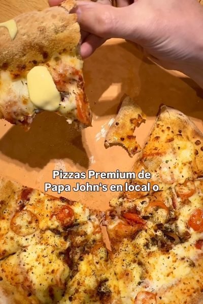Imagen de una pizza de Papa John’s, con una porción levantada y un toque de salsa, mostrando su delicioso queso y tomate