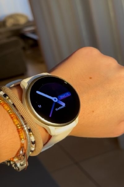 Primer plano de un reloj Garmin con una correa blanca en la muñeca, mostrando la pantalla con hora y fecha.