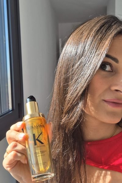Sara Barrio sosteniendo Kérastase Elixir Ultime para cabello, mostrando el producto de belleza profesional.